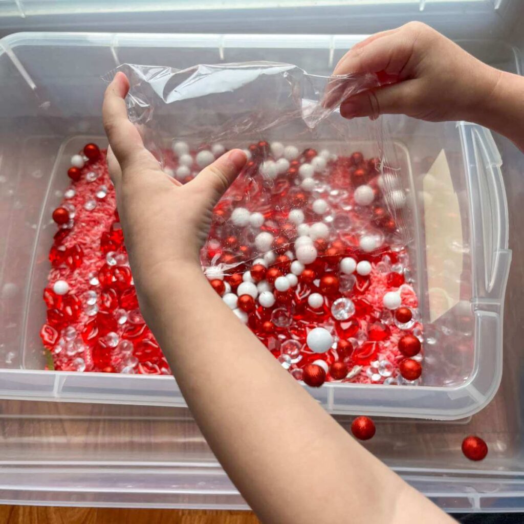 child's hands pouring red and white pom poms into bin