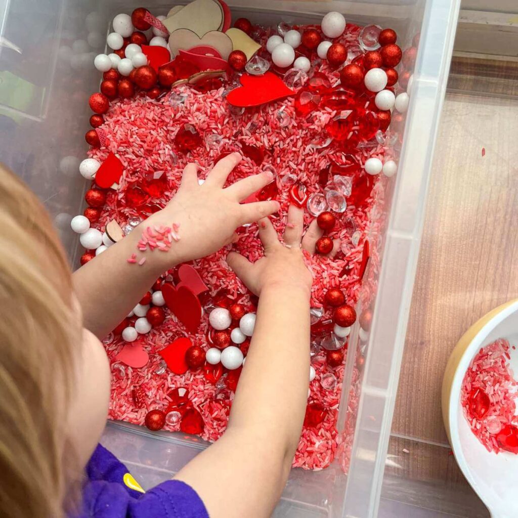 TODDLER PLAYING  IN A RED AND PINK SENSORY BIN